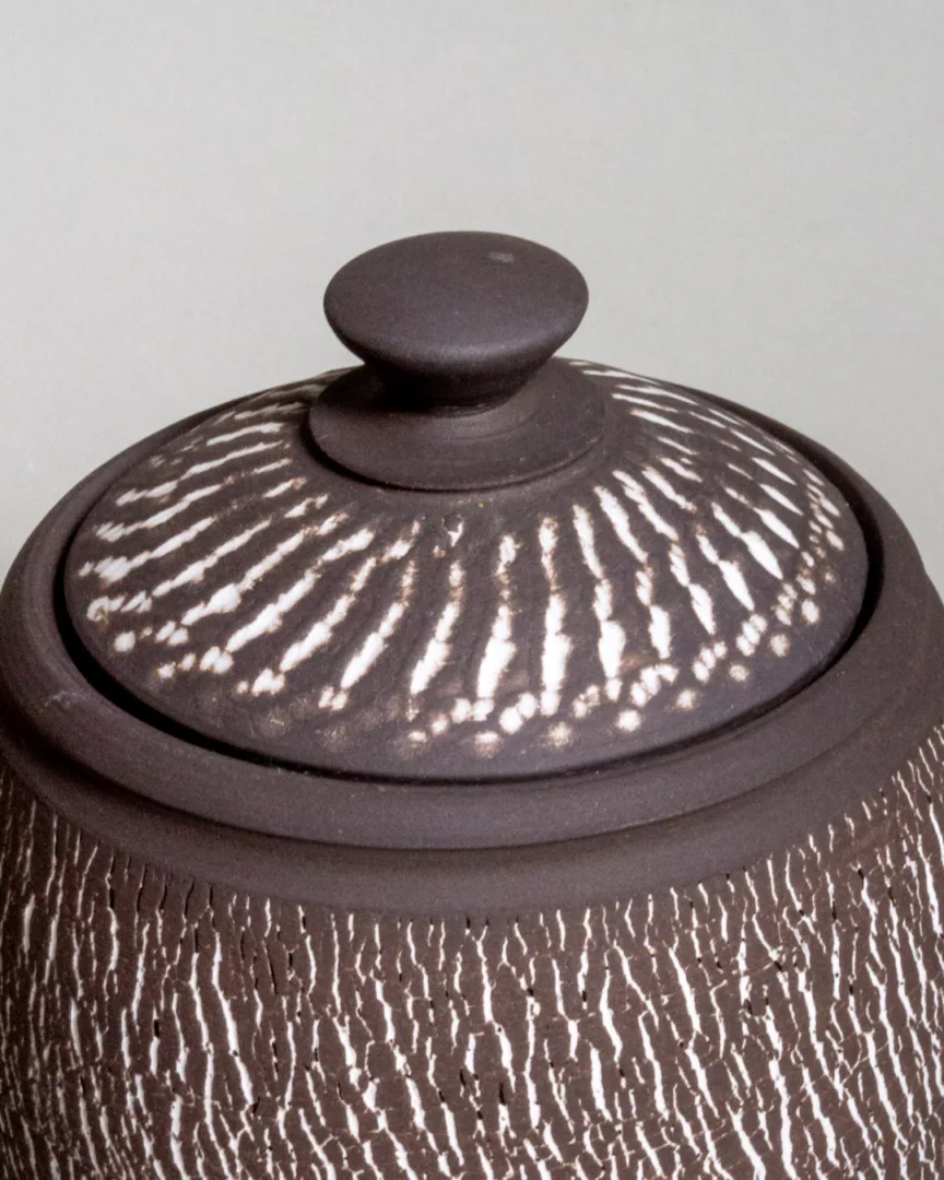 Closeup look at the black stoneware lidded jar with a white chattered and tree trunk texture
